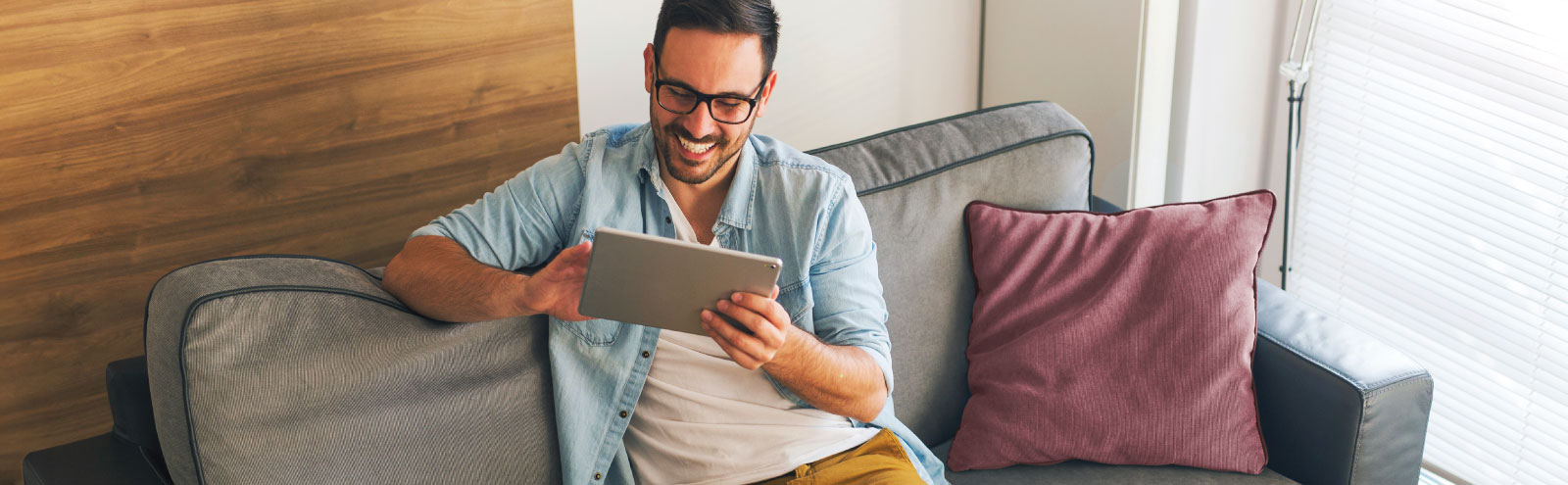 Man smiling and sitting on a couch using a tablet.