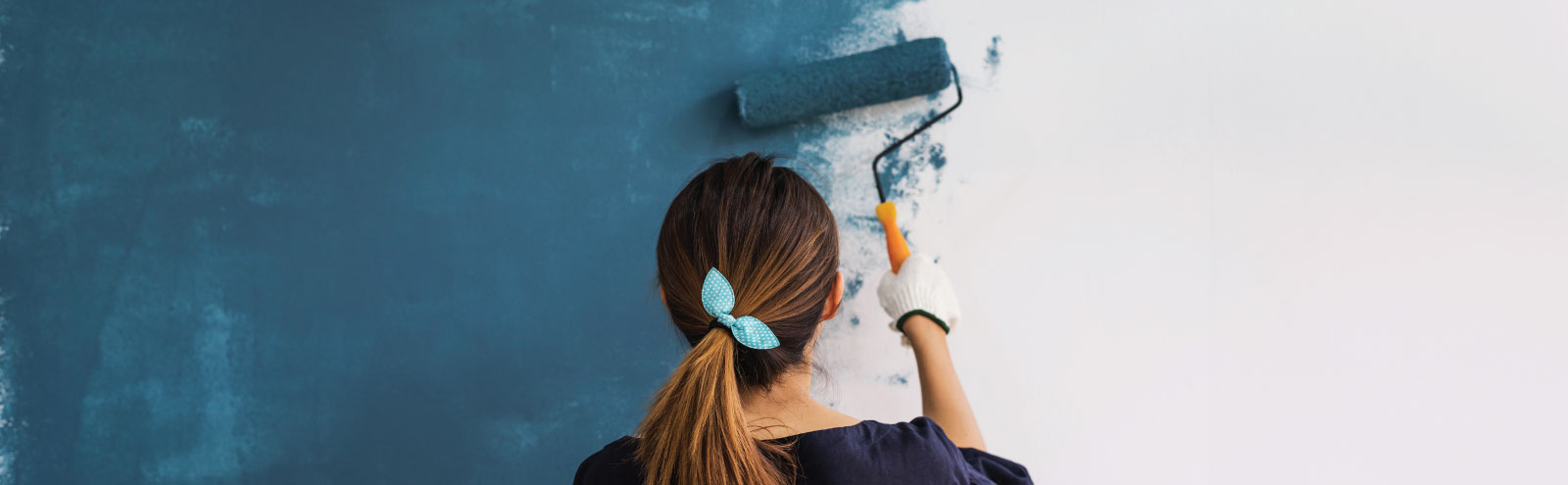 Back of woman painting wall blue.